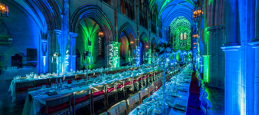Christchurch Cathedral interior at night, prepared for an event with long dining tables, illuminated by blue and green lights.