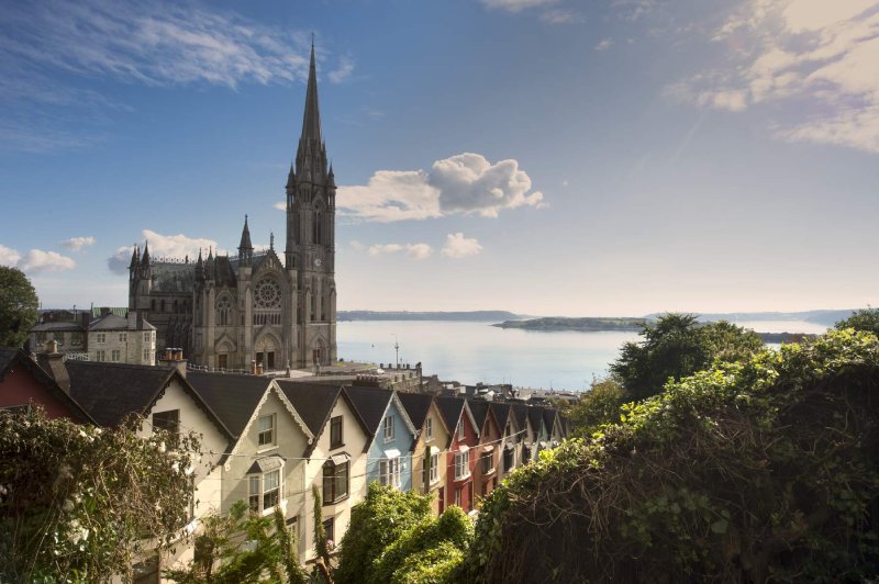 A row of colourful houses pictured in front of St. Colman's Cathedral on a sunny day in Cobh, Co. Cork.