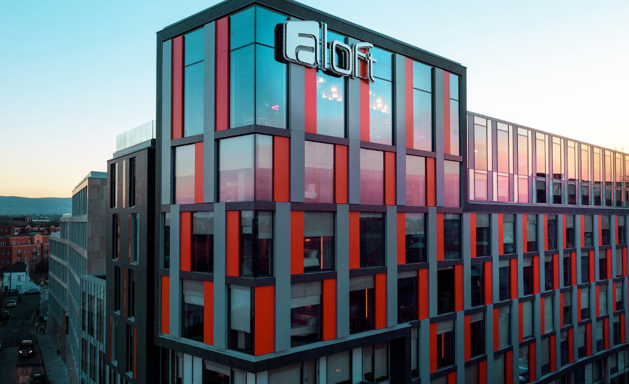 Sunset reflected in the glass, grey and red exterior of the Aloft hotel