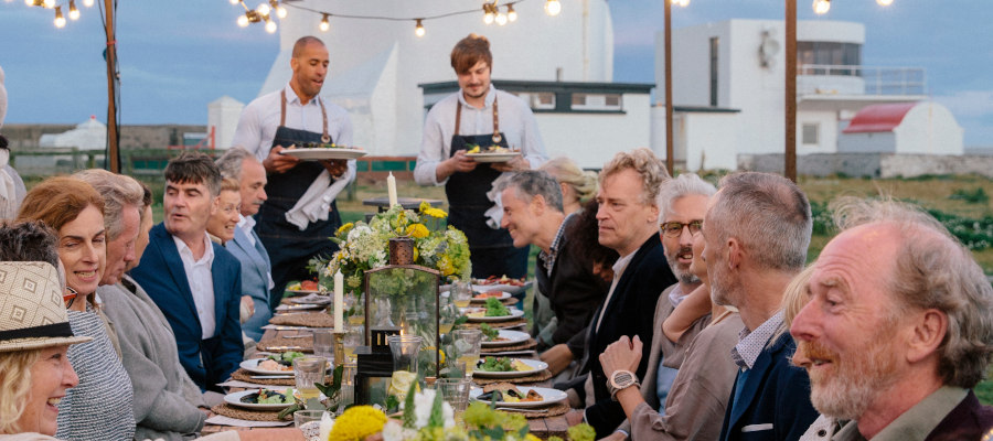 Group of people enjoying dinner at outdoor table near lighthouse