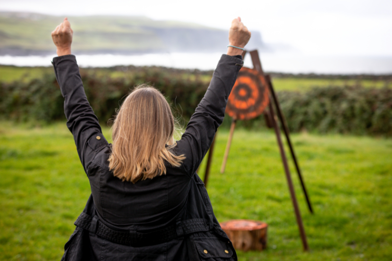 A woman raises her hands in triumph from hitting the target through the activity axe throwing.