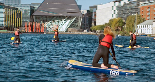 Delegates in life jackets, paddle boarding in a body of water