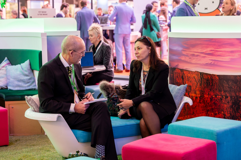 Two people sitting on a colourful couch, having a business conversation at IBTM World 2023