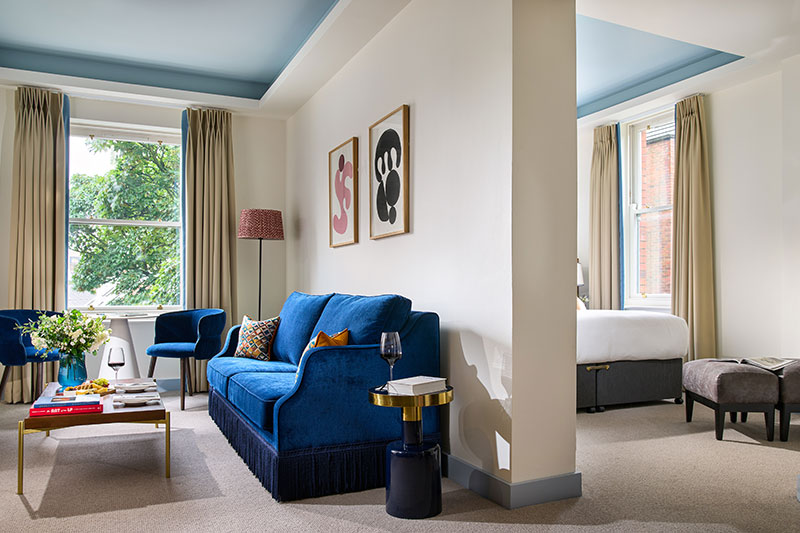 Spacious hotel suite with blue furniture and bright natural lighting