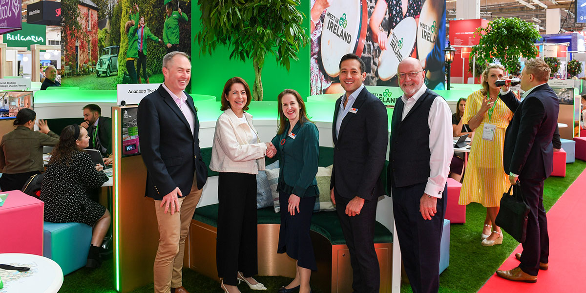 A group of MICE industry professionals posing at a conference in front of a stand that says "Meet in Ireland"