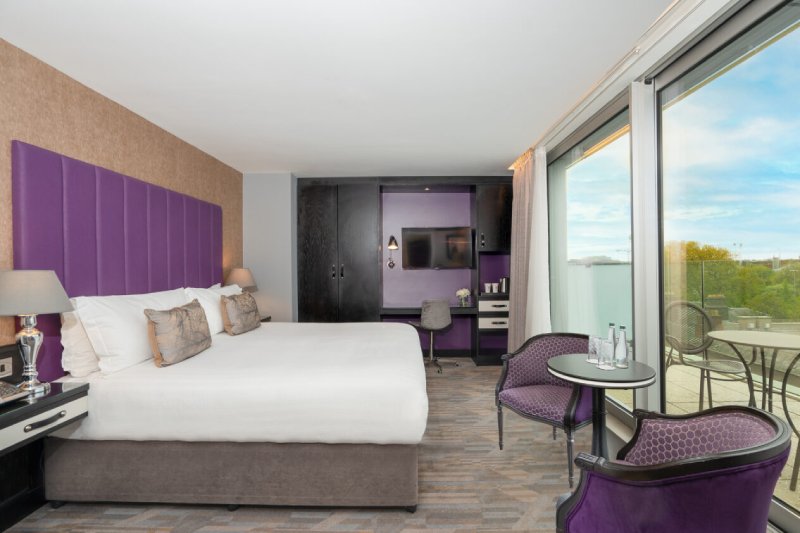 Spacious Deluxe King Balcony Room at Trinity City Hotel, featuring a modern design with purple accents and a private outdoor seating area