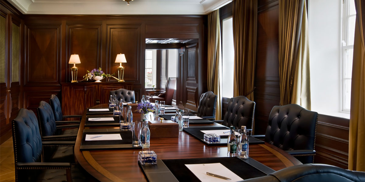 Conference table surrounded by leather chairs in a wood panelled room with large windows