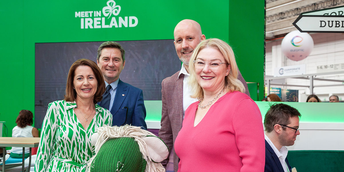 Group of people posing in front of the Meet in Ireland event stand with a green background