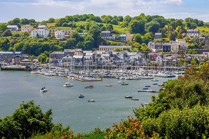 Scenic view of a marina in Kinsale with boats docked and colourful buildings on a hillside in the background