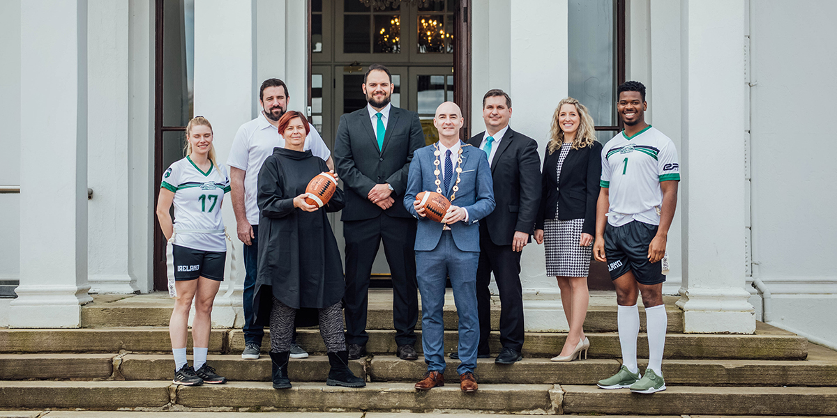 Group of people posing on steps holding American footballs.