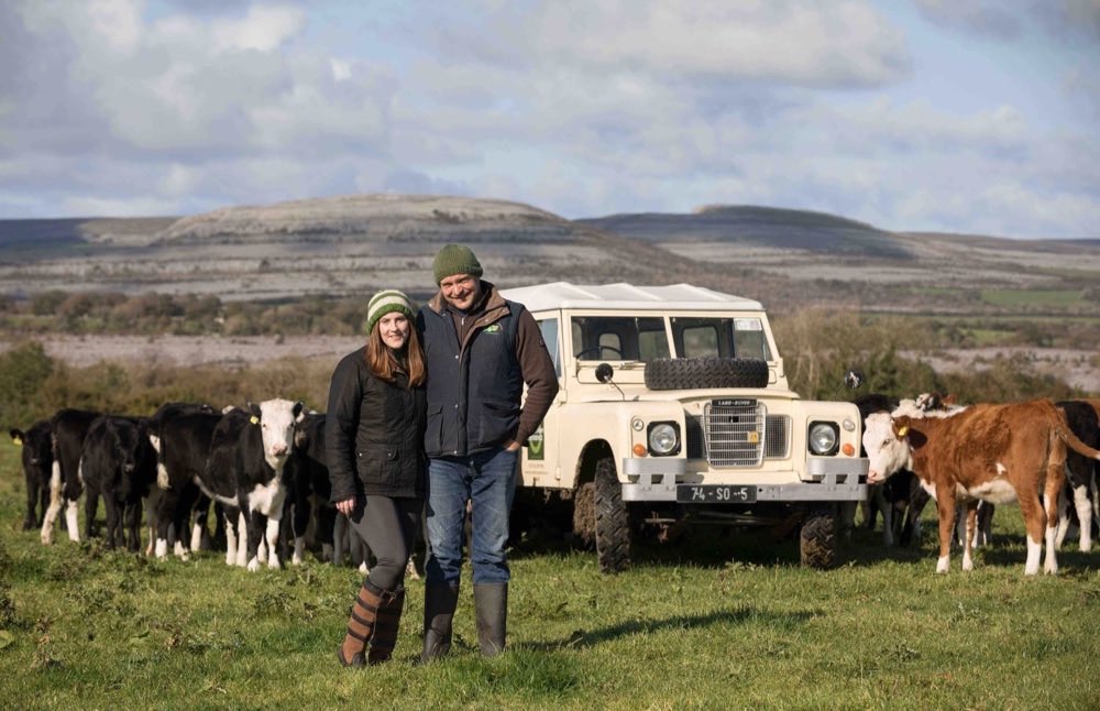 Two farmers standing in a field with cars