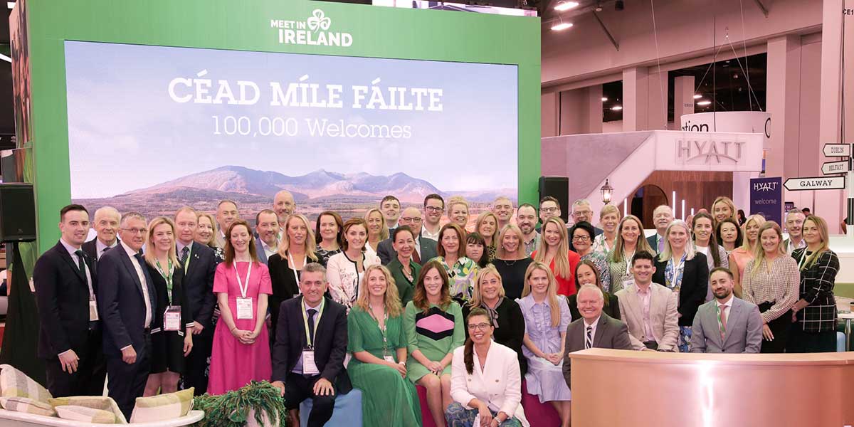 Large group of people posing in front a green backdrop