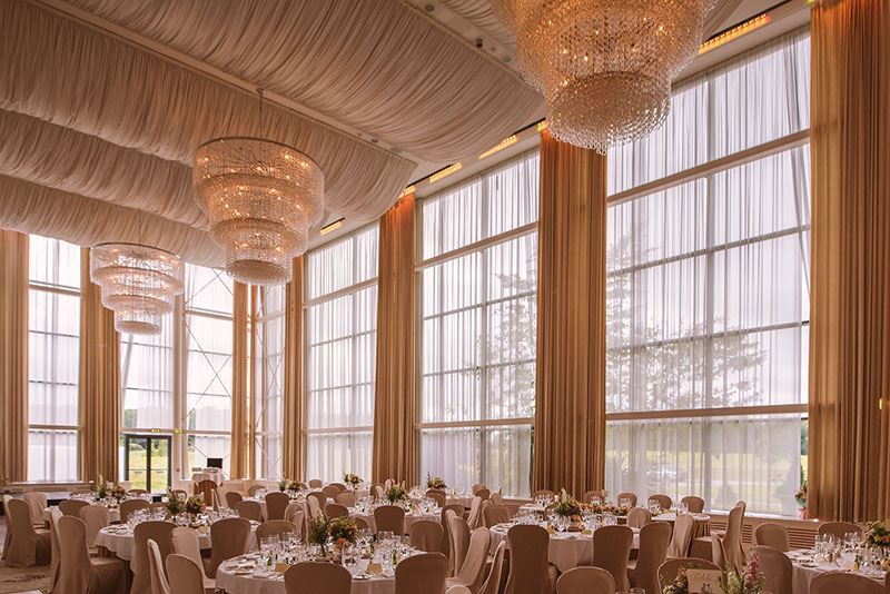 A large ballroom with tall windows and chandeliers, set up for a formal event