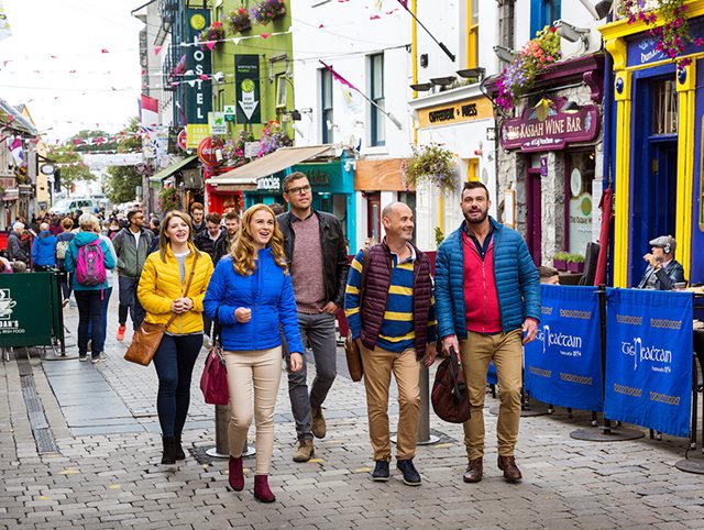 Five delegates walk past pubs and small shops along the narrow streets in Galway