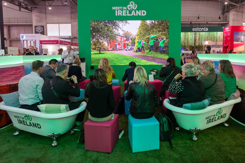 Group of attendees seated in bathtubs and stools, watching a presentation at the Meet in Ireland event booth