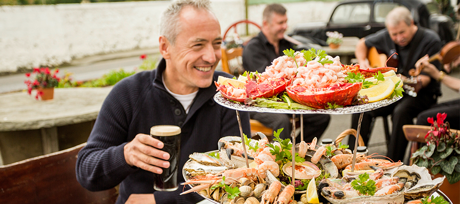 Man holding pint of Guinness beside platter of fresh seafood