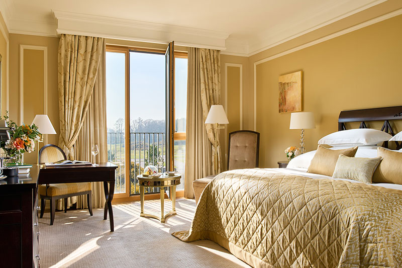 Luxurious hotel bedroom with gold decor and a view out to a garden