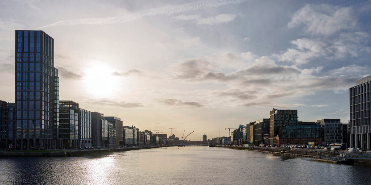 Sunset view of Dublin Docklands with modern buildings lining both sides of the river and the Samuel Beckett Bridge visible in the distance
