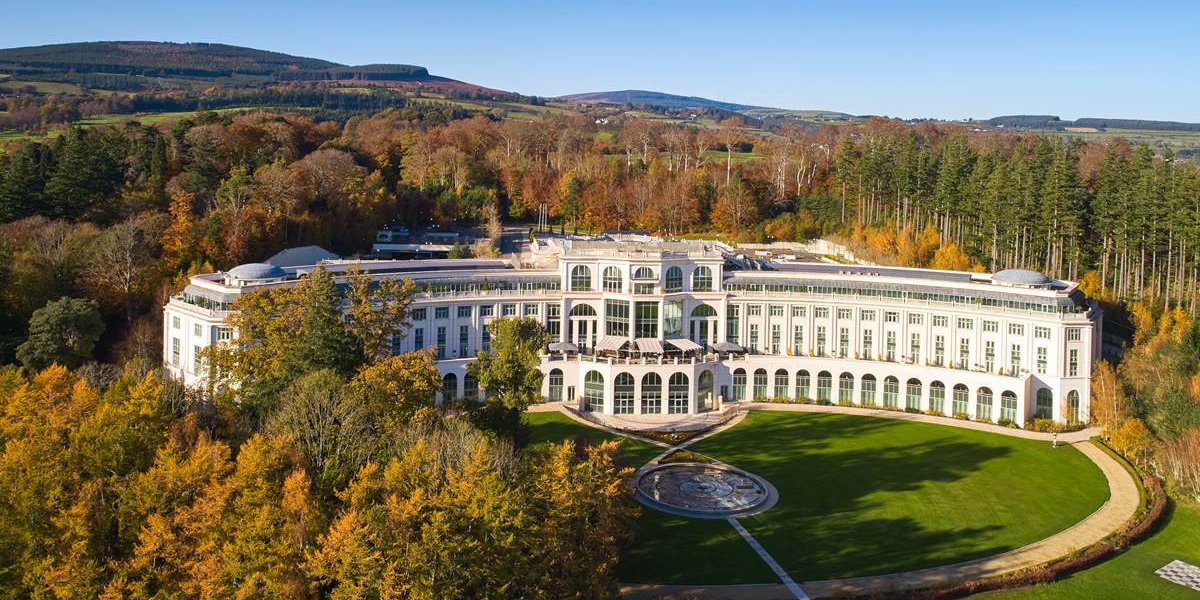 Powerscourt Hotel Estate surrounded by autumnal trees with a blue sky in the background