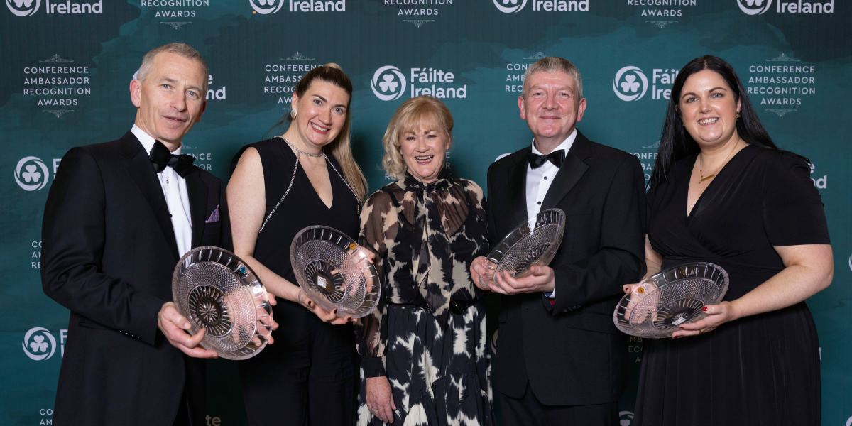 Group of people holding awards and standing in front of a dark green background with the Fáilte Ireland logo on it